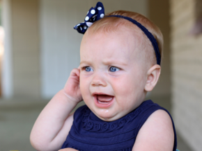 Baby in blue dress crying and pulling on ear