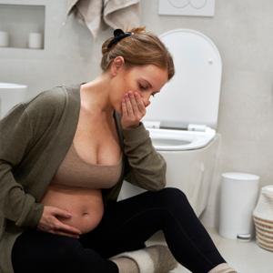 Pregnant lady sitting on the ground in a bathroom with her hand over her mouth