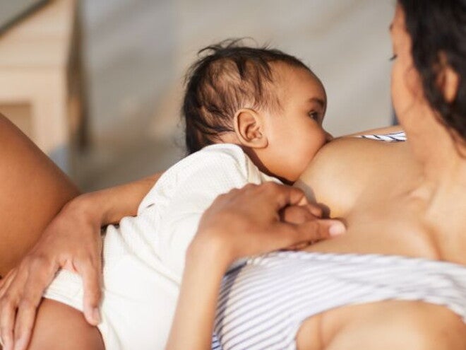 Mother in striped top breastfeeding her baby in a white onesie 