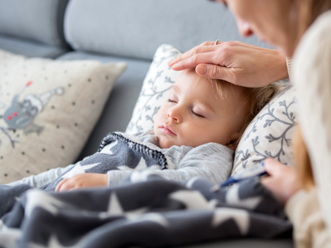Toddler laying down with mothers hand on toddlers head
