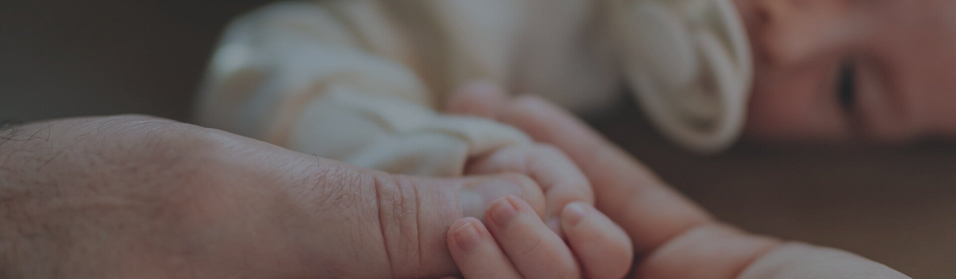 Parents holding their new babies hand while they lie down